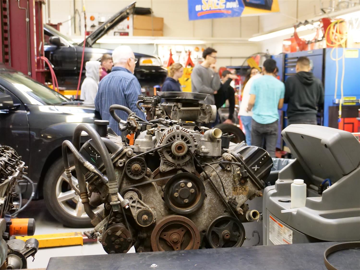 Cars on a lift and students working in the CHS auto shop. Car engine in foreground